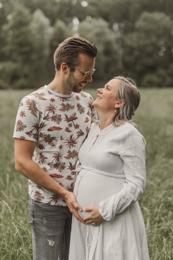 Paar lacht mit Babybauch in der Natur