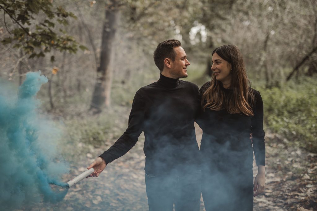 Mann und Frau stehen in der Natur mit Babybauch und Rauchbombe