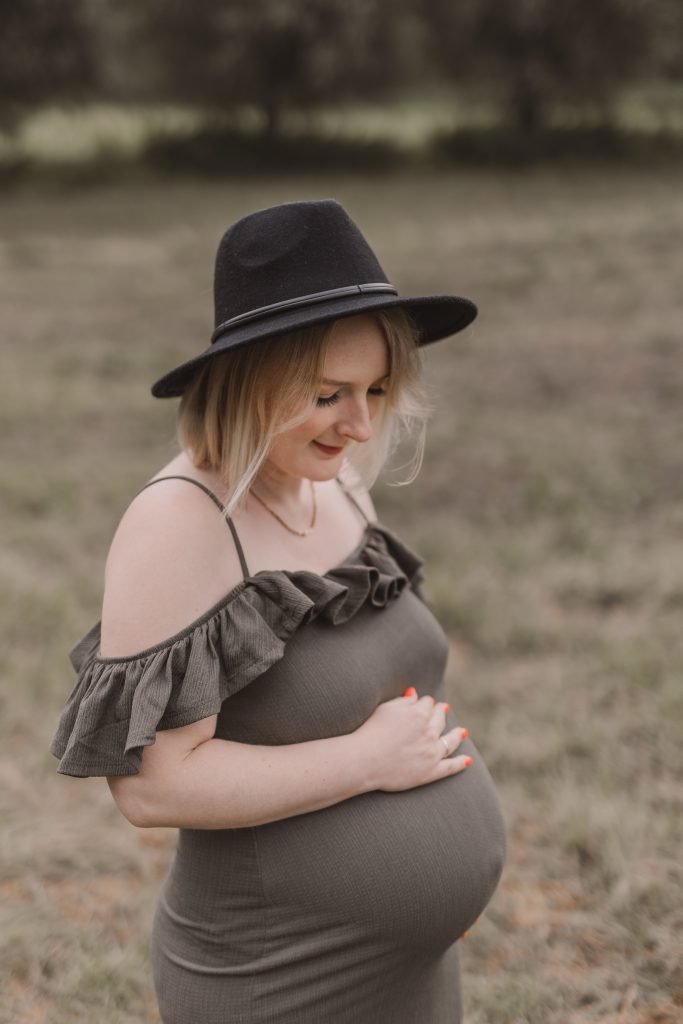 Schwangere Frau mit Hut streichelt ihren Babybauch