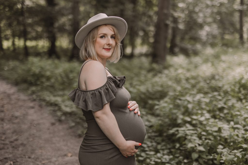 Schwangere Frau steht in der Natur mit Babybauch und Hut