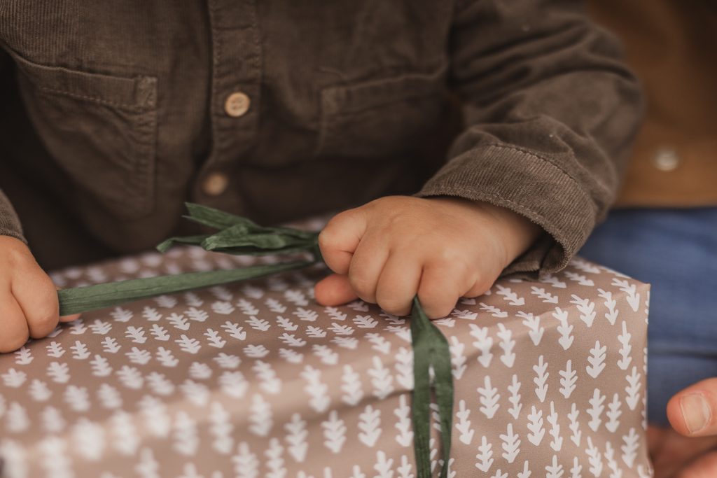 Kleine Kinderhände die ein Geschenkband an einem Weihnachtsgeschenk auspacken